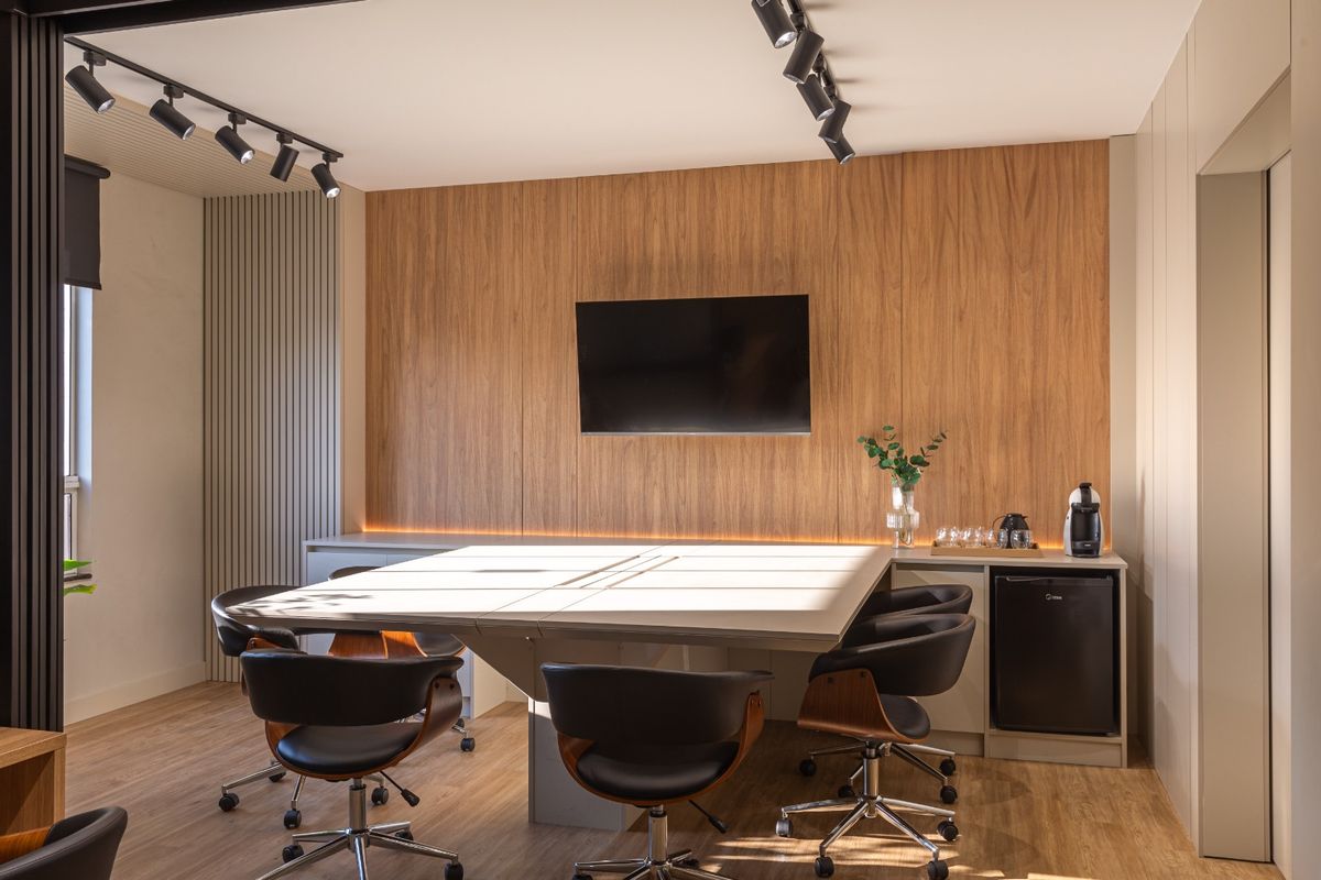 Sala de reunião com mesa ampla, televisão e painel de madeira